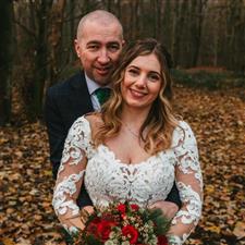 Smiling groom hugs bride from behind in wooded autumnal scene