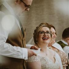 Glasses wearing bride smiles up at her husband while he gives his speech