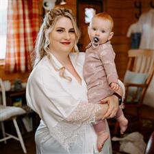 Blonde bride holds her baby while both looking at the camera