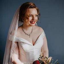 Bride with red lipstick smiles off camera wearing white wedding dress and long veil