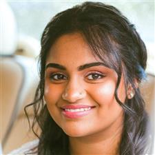 Indian bride with black hair smiles at the camera with winged eyeliner, pink eyeshadow and lipstick