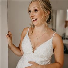 Pregnant bride in white dress holds her bump and smiles off camera in surprise