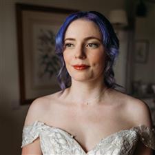 Purple haired bride looks off camera wearing delicate necklace