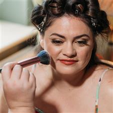 Bride with hair in pin curls gets blusher applied