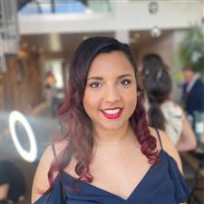 Bridesmaid wearing deep blue dress smiles into camera with bright red lip and matte skin